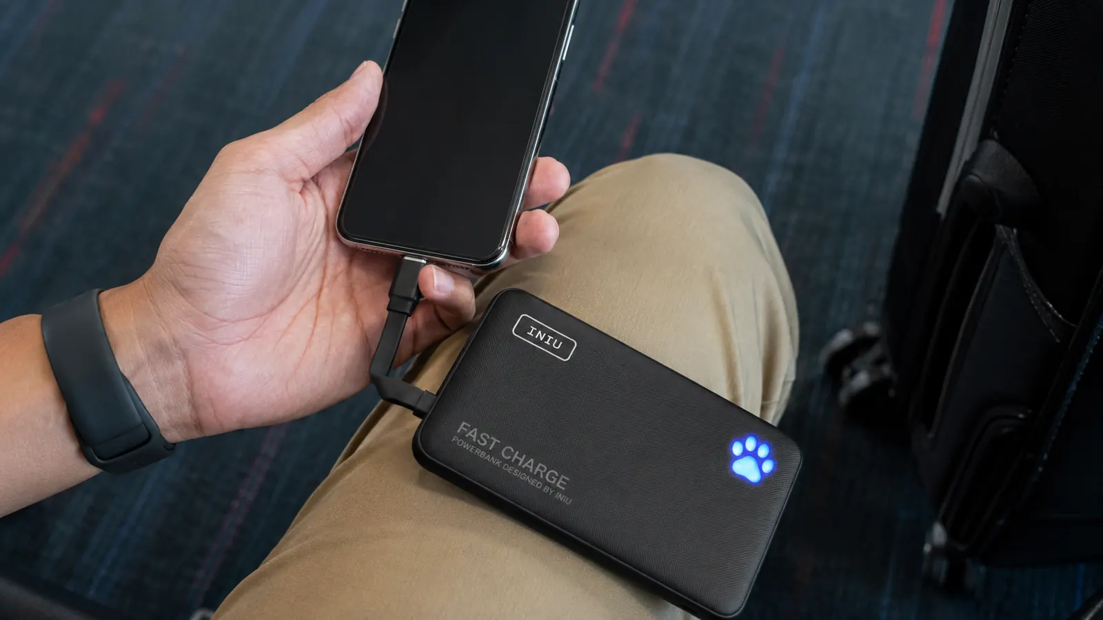 Close-up of a hand plugging a phone into the INIU power bank's built-in USB-C cable at an airport seat