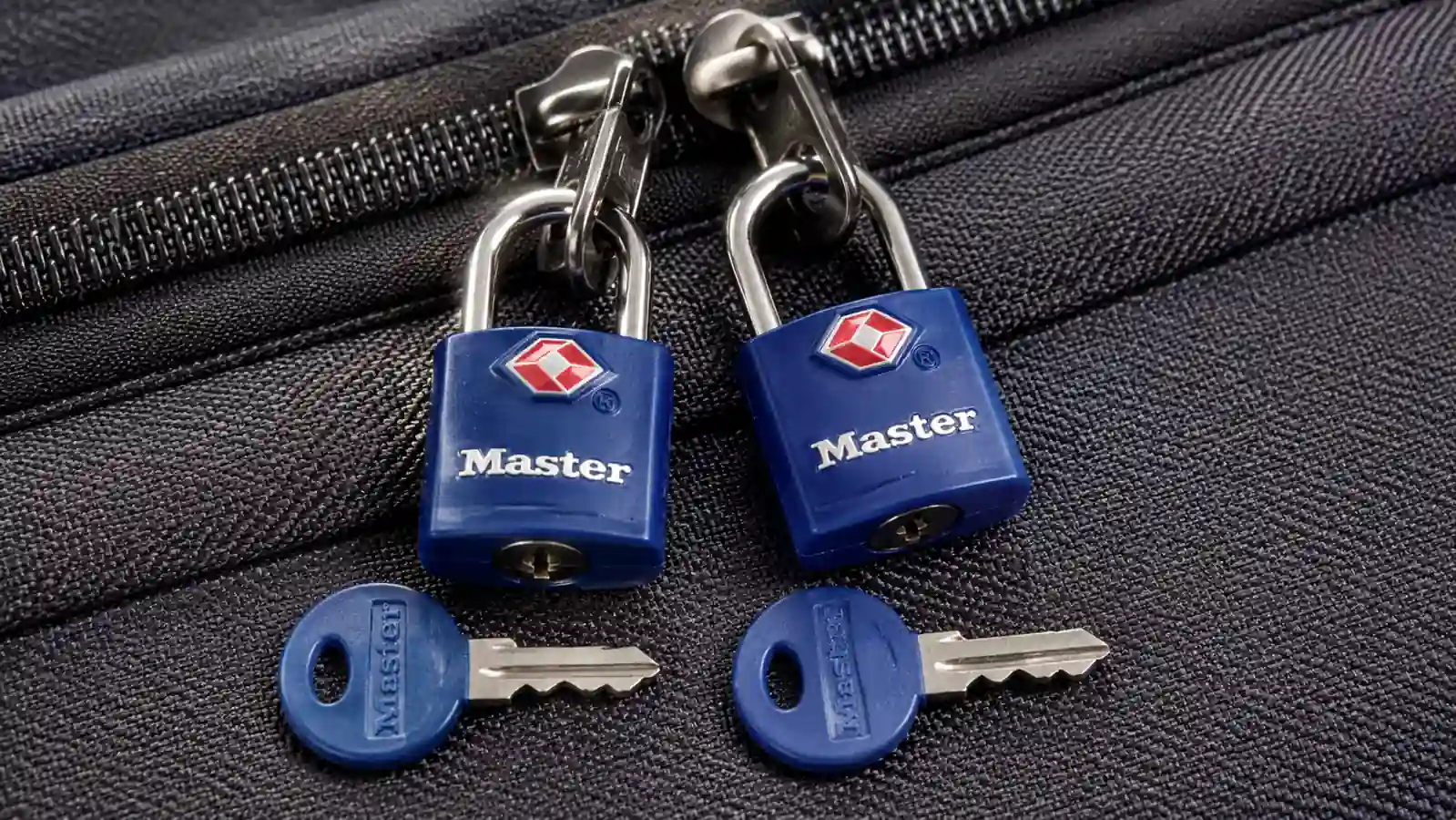 Close-up of two Master Lock keyed padlocks side by side on a suitcase, each with its own separate key