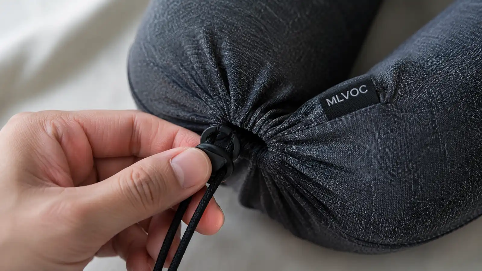 Close-up of a hand pulling the elastic compression strap tight around a folded memory foam neck pillow