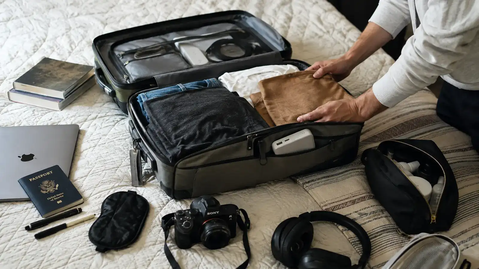 A carry-on bag open on a bed with a packing cube, toiletry bag, and a power bank tucked into a front pocket